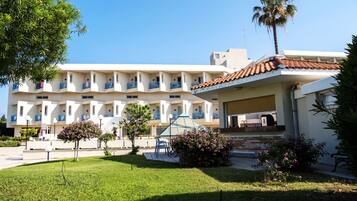 Un hotel de varios pisos con balcones, un área de estar exterior cubierta y un césped bien cuidado.