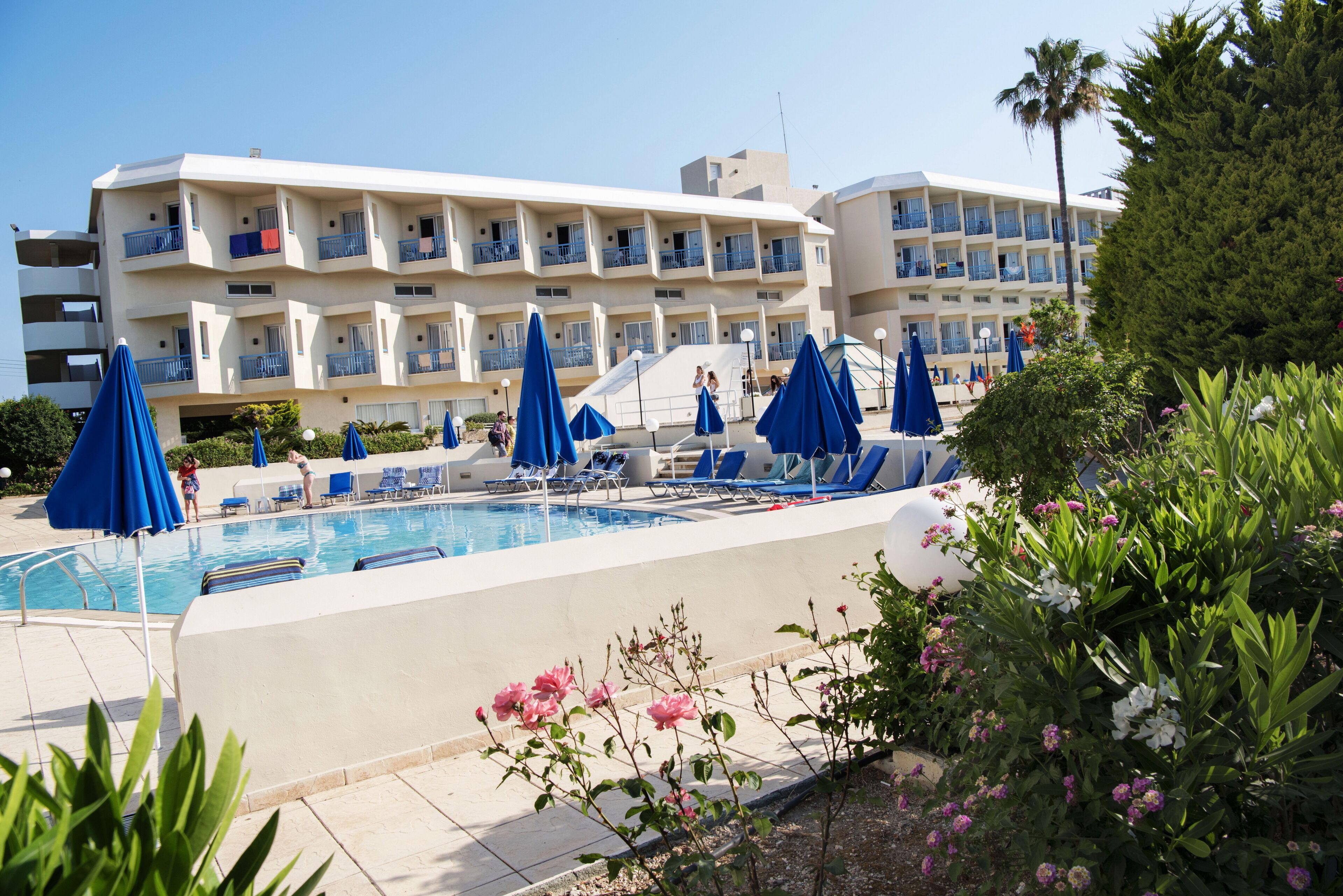 Un hotel con piscina, sombrillas azules y un edificio de varios pisos con balcones.