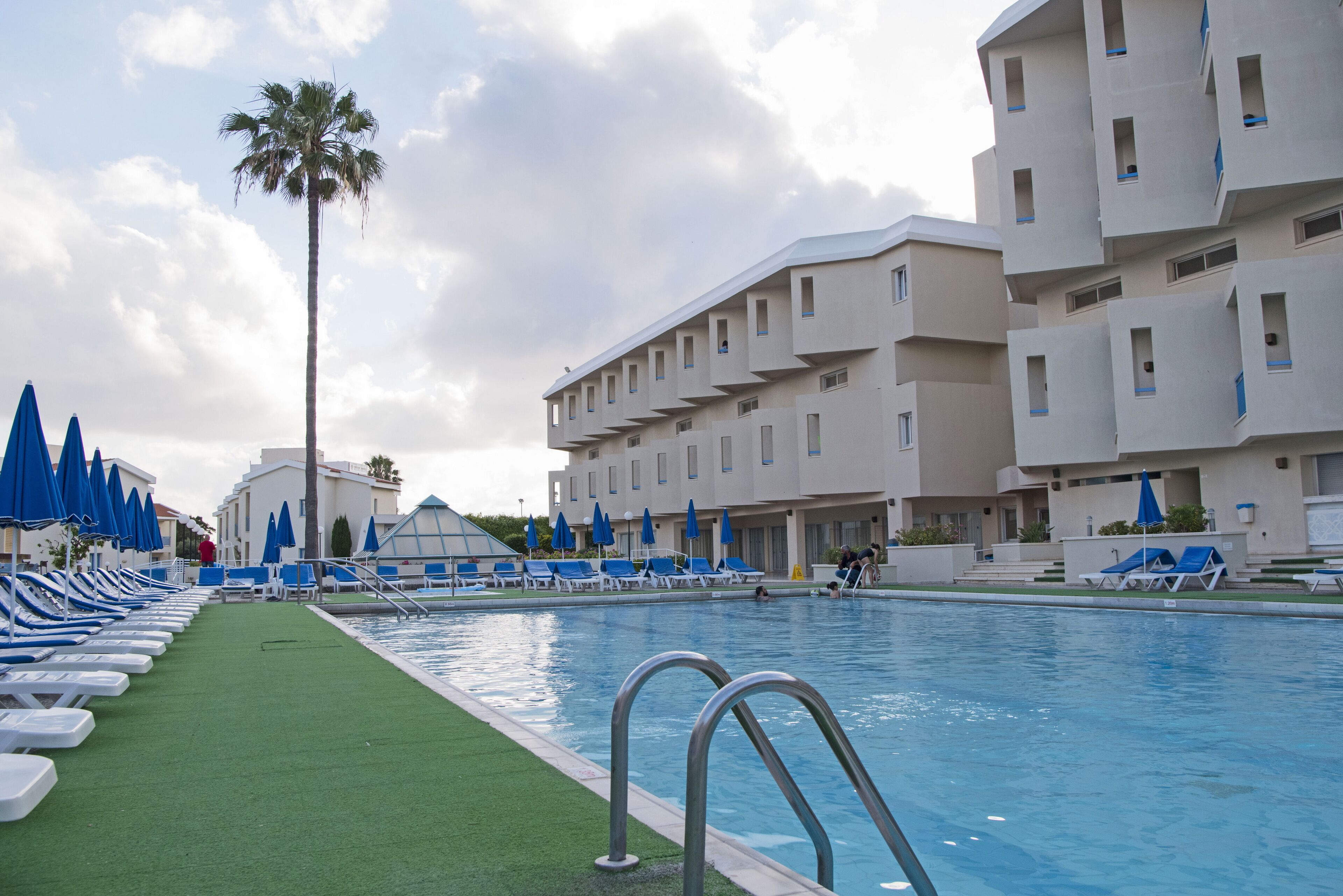 A swimming pool area with blue umbrellas, lounge chairs, and a palm tree.
