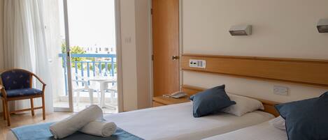 A hotel room with a bed, a chair, a table, and a balcony with a railing.