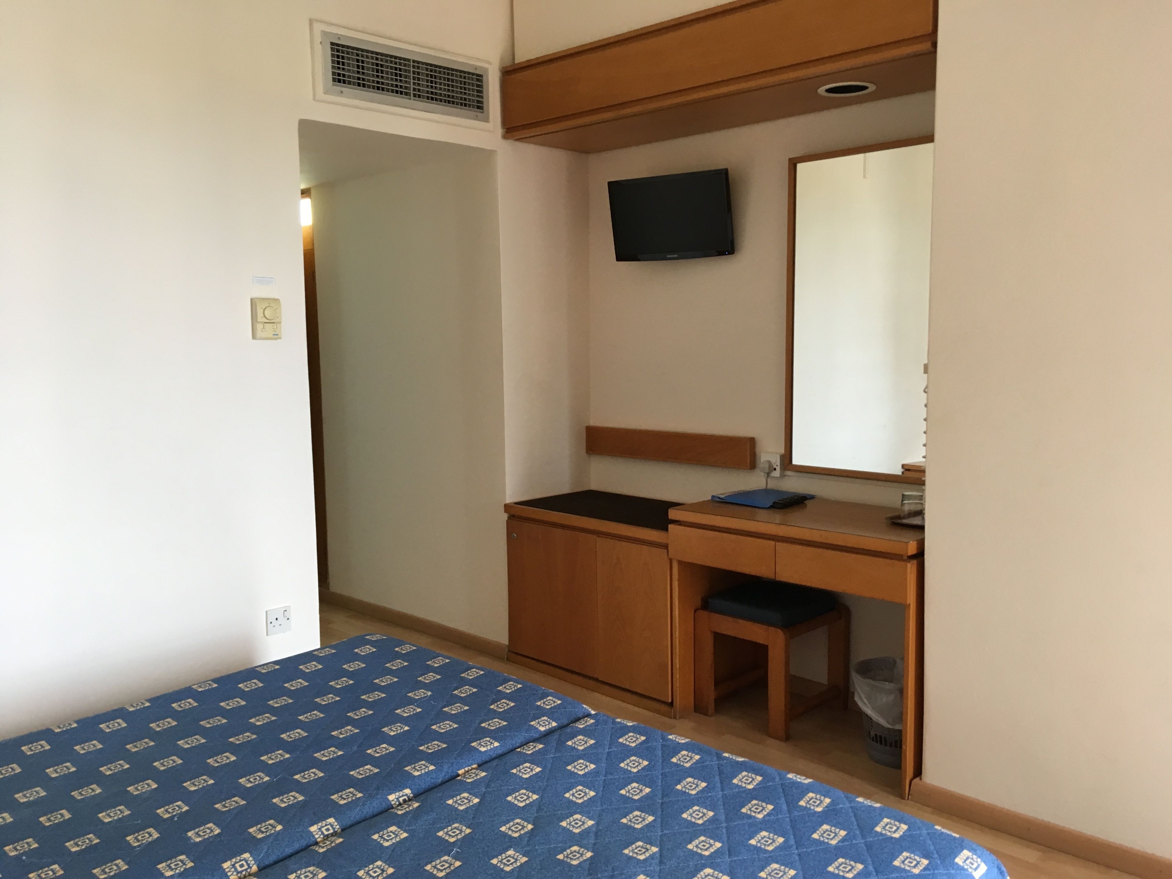 Un dormitorio con cama, escritorio, silla, televisor y espejo.
