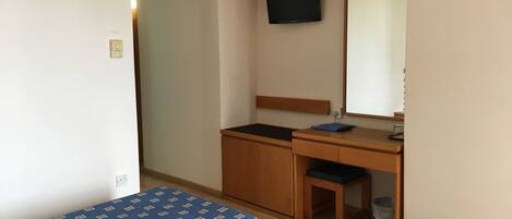 Un dormitorio con cama, escritorio, silla, televisor y espejo.