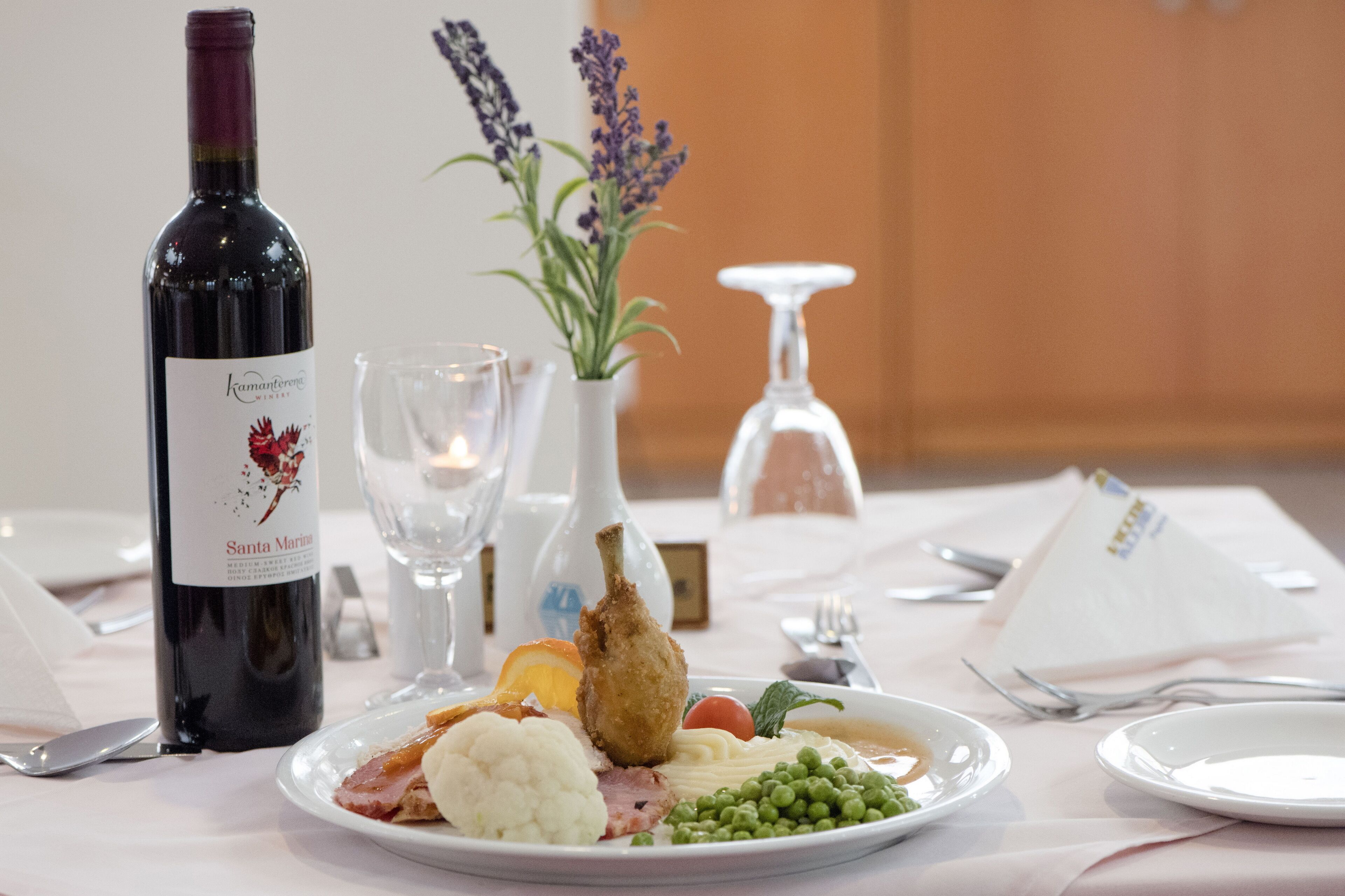 A table set with a bottle of wine, a glass, a vase with flowers, and a plate of food.