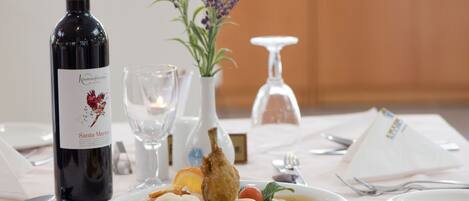 A table set with a bottle of wine, a glass, a vase with flowers, and a plate of food.