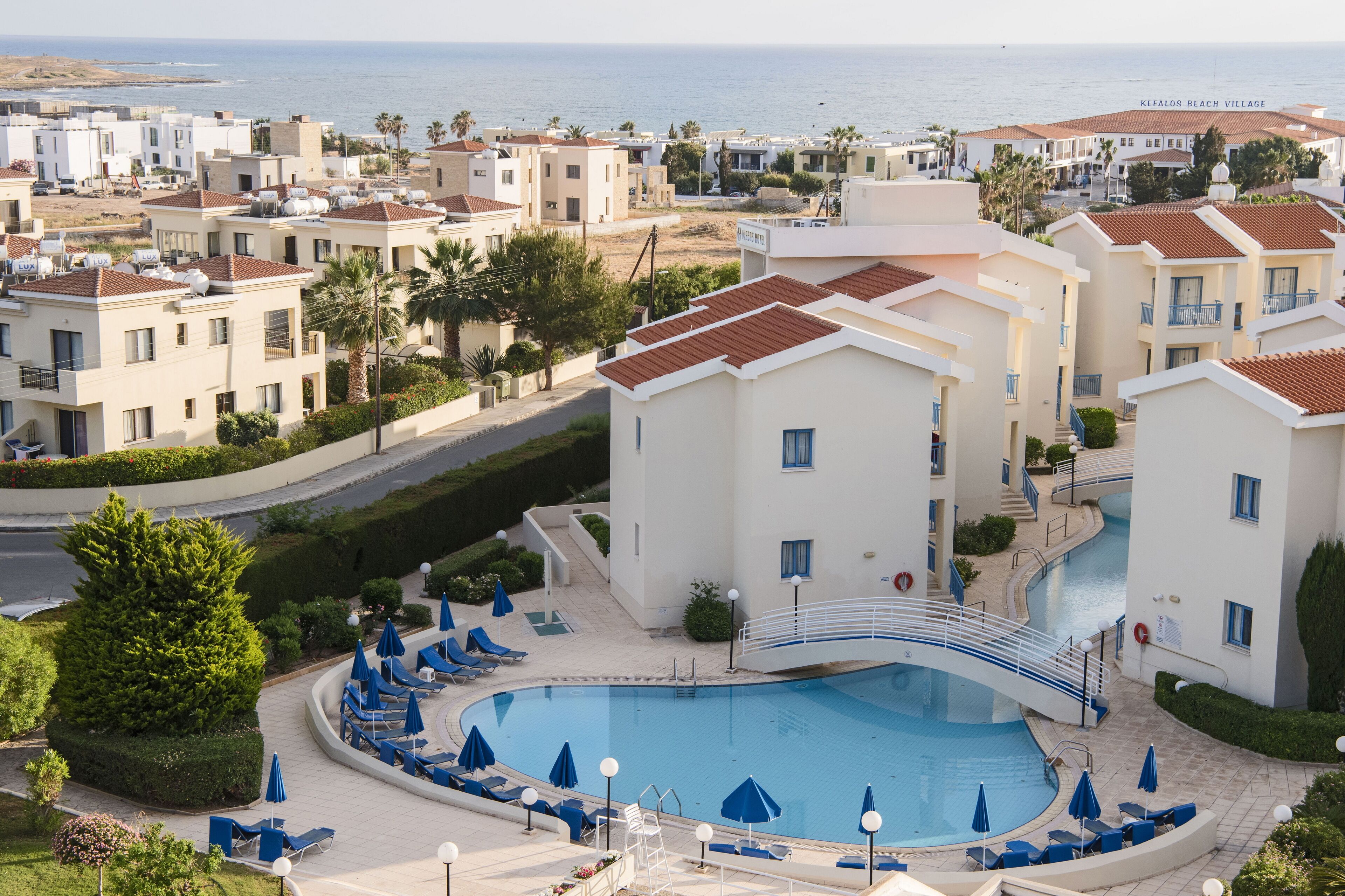 Un resort con piscina rodeada de sillones y sombrillas, un sendero curvo y vista al mar.