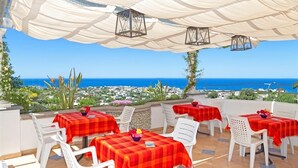 An outdoor terrace with tables and chairs, overlooking a coastal cityscape.