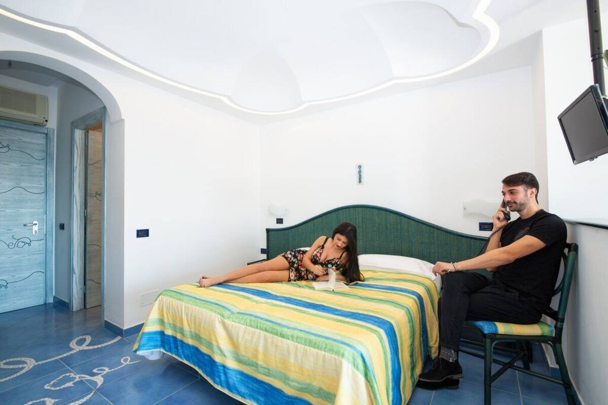 A hotel room with a bed, a chair, and a TV mounted on the wall.