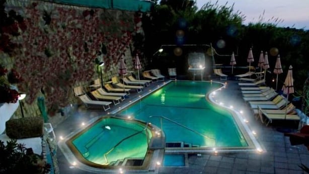 A swimming pool with multiple lanes, surrounded by lounge chairs and umbrellas, set against a landscaped backdrop.