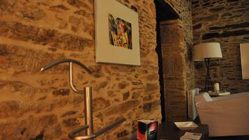 A room with a stone wall, a framed picture, a lamp, and a bed.