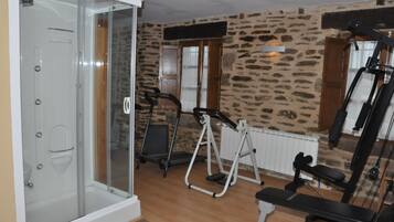 Un gimnasio con pared de piedra, cinta de correr, elíptica y banco.