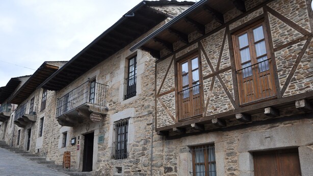 A row of stone buildings with wooden balconies and windows.