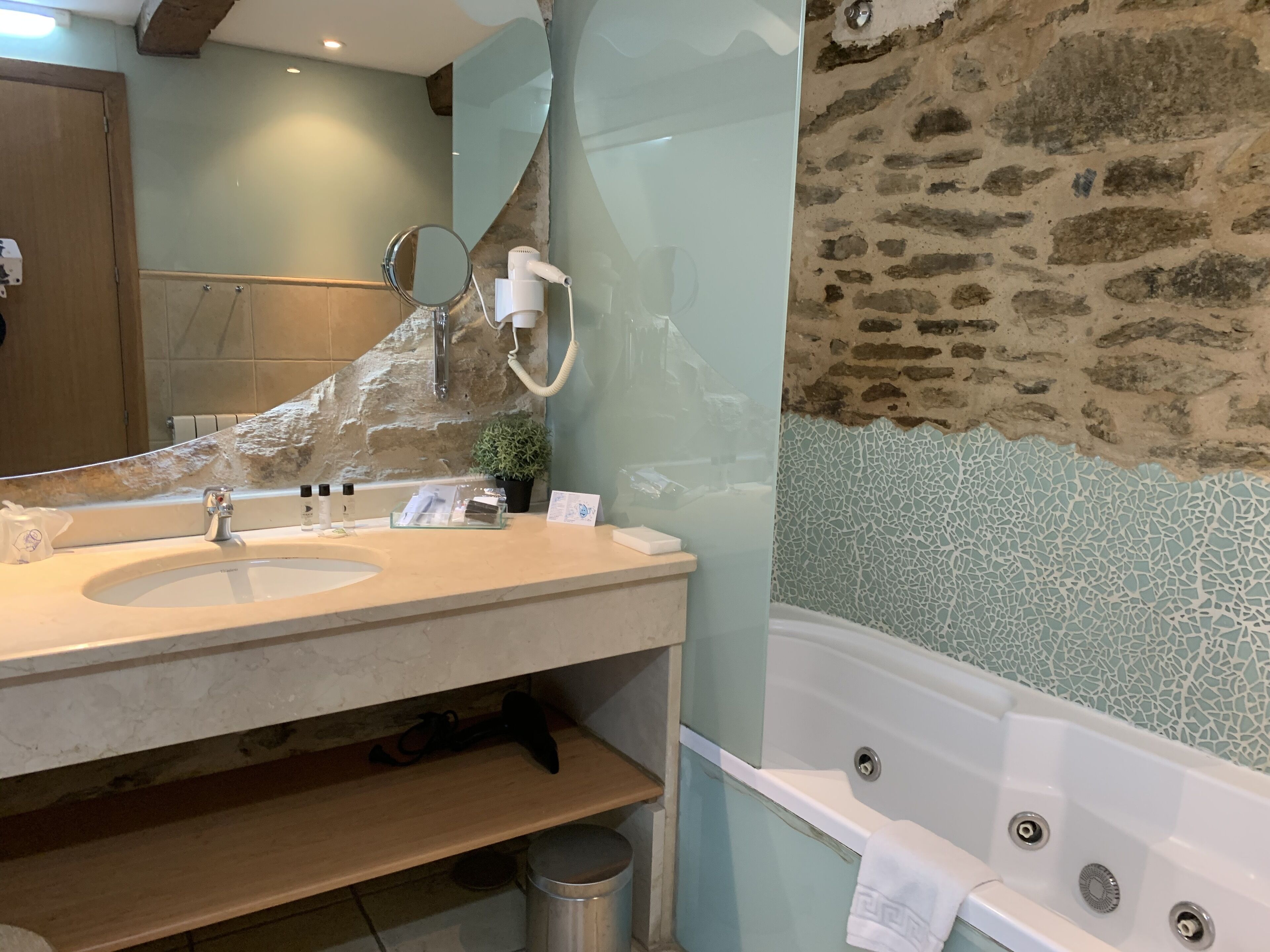 Une salle de bain avec un mur en pierre, une baignoire, un lavabo avec des articles de toilette et un miroir.