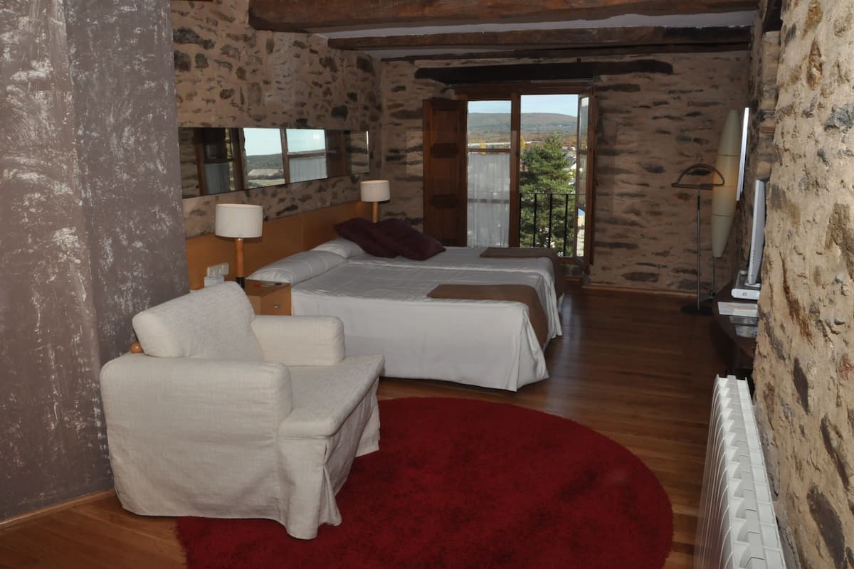 A bedroom with two beds, a red rug, a white armchair, and a stone wall.