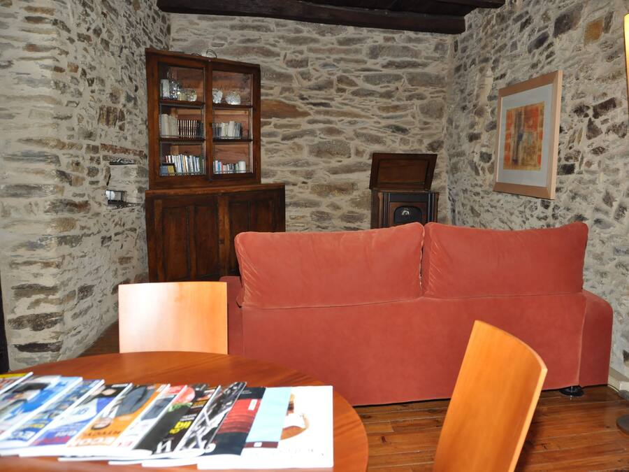 A room with a stone wall, a wooden cabinet with glass doors, a red sofa, a table with magazines, and a floor lamp.