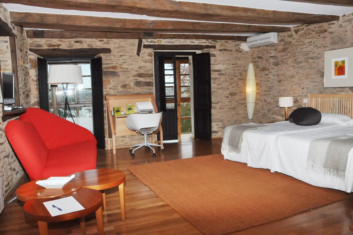 A room with a bed, a red chair, a desk with a chair, and a window.