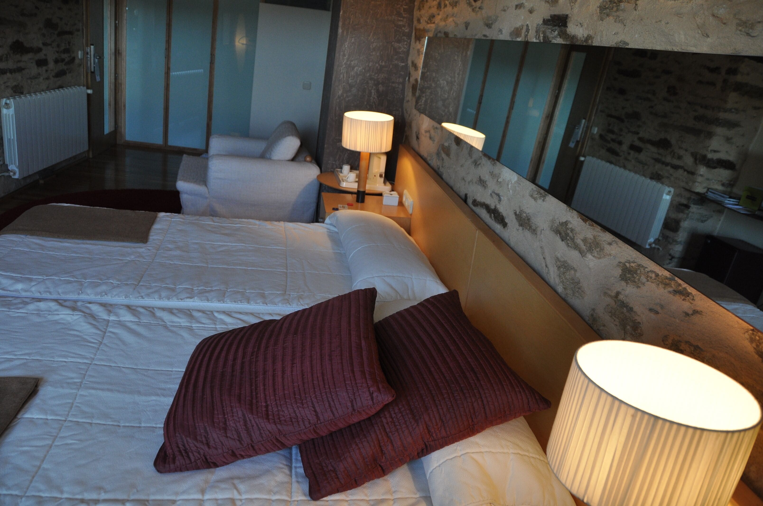 Een hotelkamer met twee bedden, een nachtkastje met een lamp en een stenen muur.