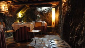 A rustic dining area with stone walls, wooden benches, and tables set for a meal.