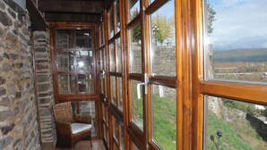 A room with stone walls, wooden floors, and large windows offering a view of a hillside.