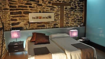 Un dormitorio con pared de piedra, cama con dos almohadas, mesita de noche con lámpara y un cuadro en la pared.
