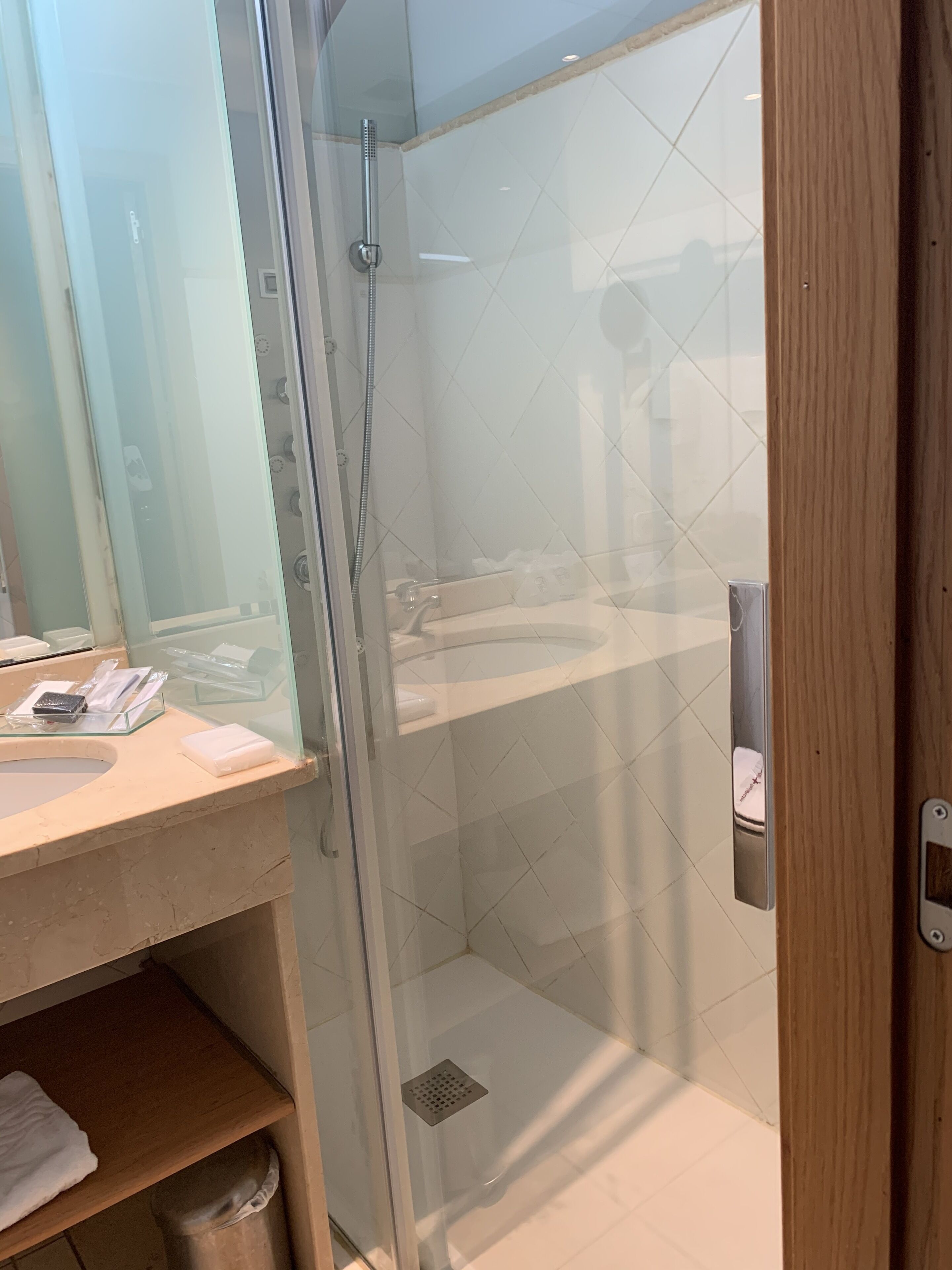 A glass-enclosed shower stall with a white tiled floor, a wooden door, and a glass shower door.