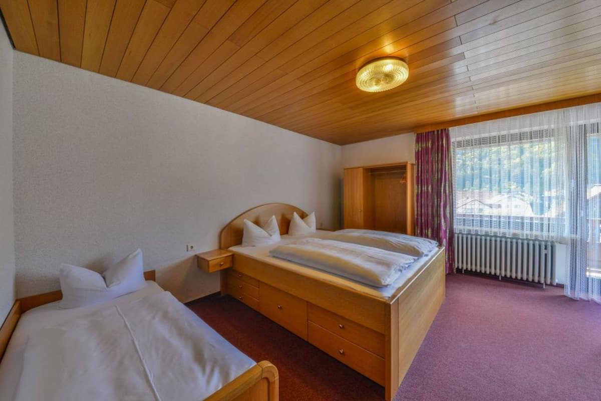 Ett hotellrum med ett träpanelat tak, en säng med vita sängkläder, en byrå i trä och ett fönster med gardiner.