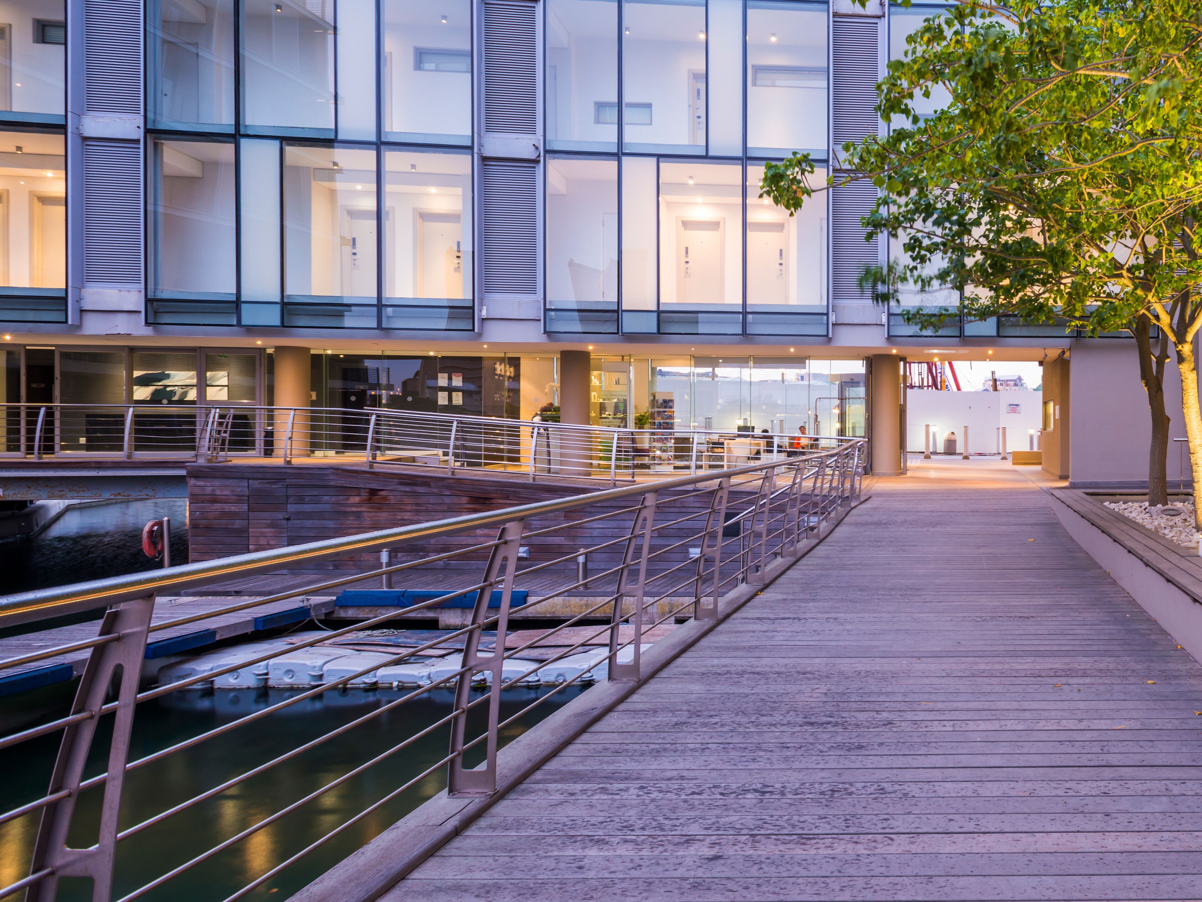 Een modern gebouw met grote ramen, een houten terras en een waterpartij.