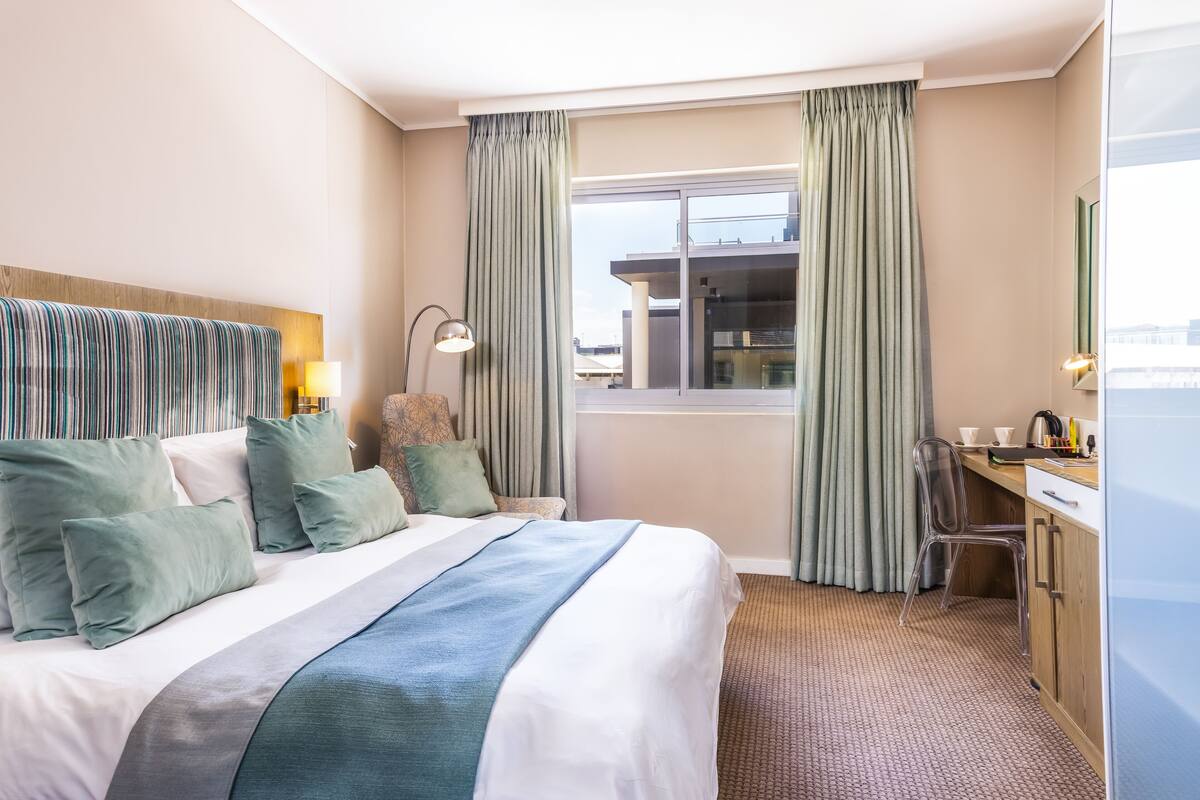 A hotel room with a large bed, a desk, and a window with curtains.
