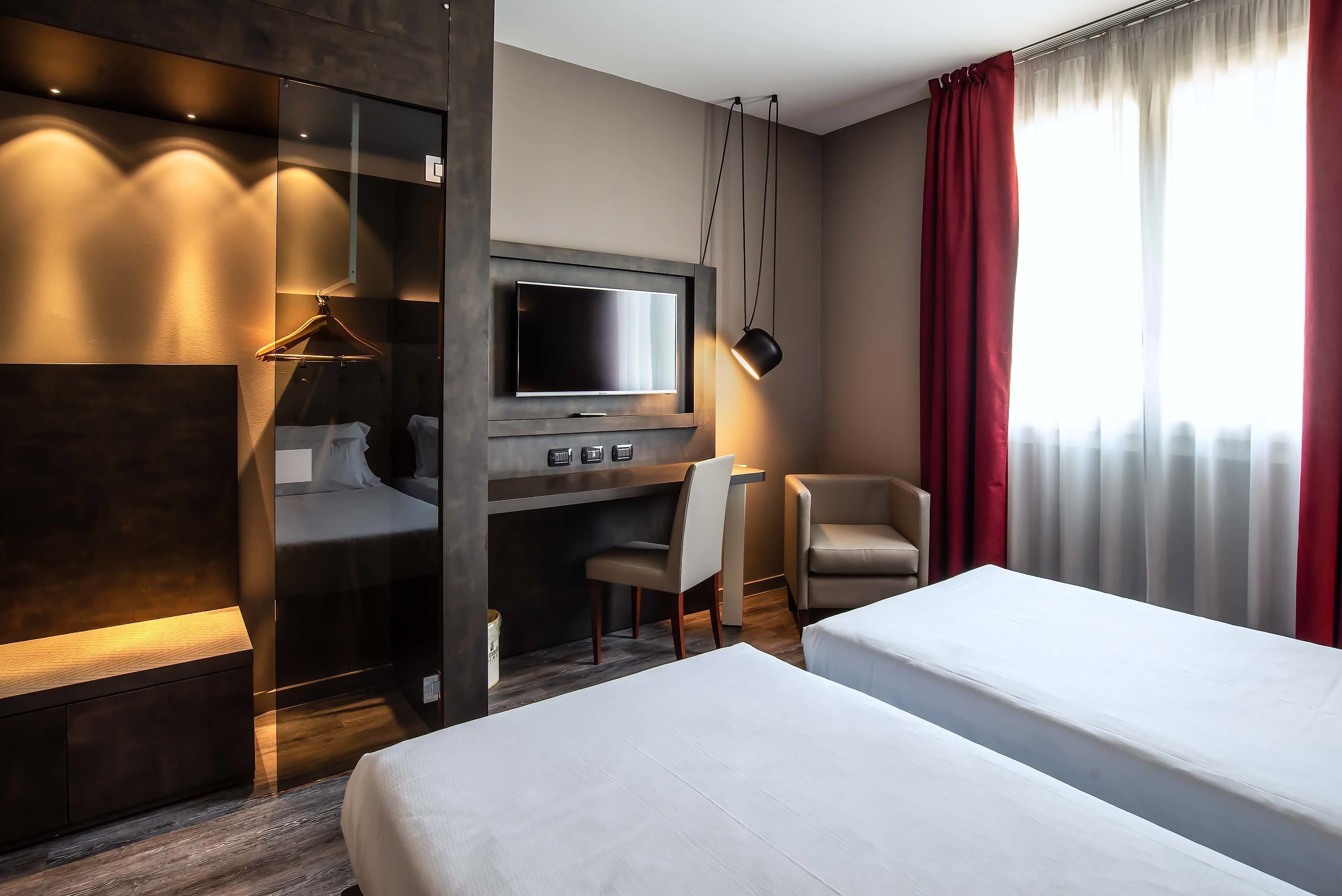 A hotel room with a bed, a desk, a chair, a TV, and a wardrobe.