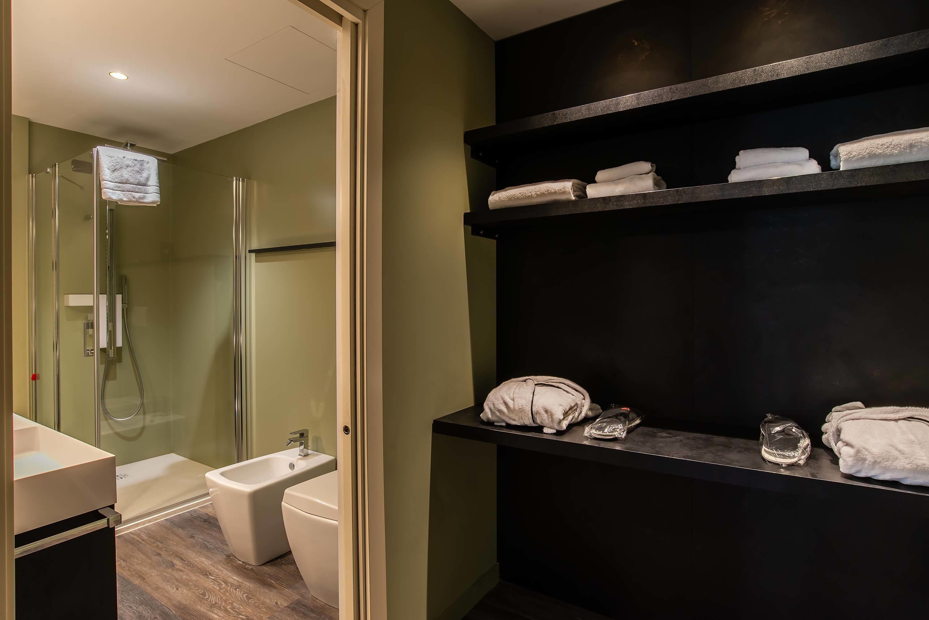 Un baño moderno con cabina de ducha de vidrio, un bidé, un lavamanos y un estante con toallas dobladas ordenadamente.