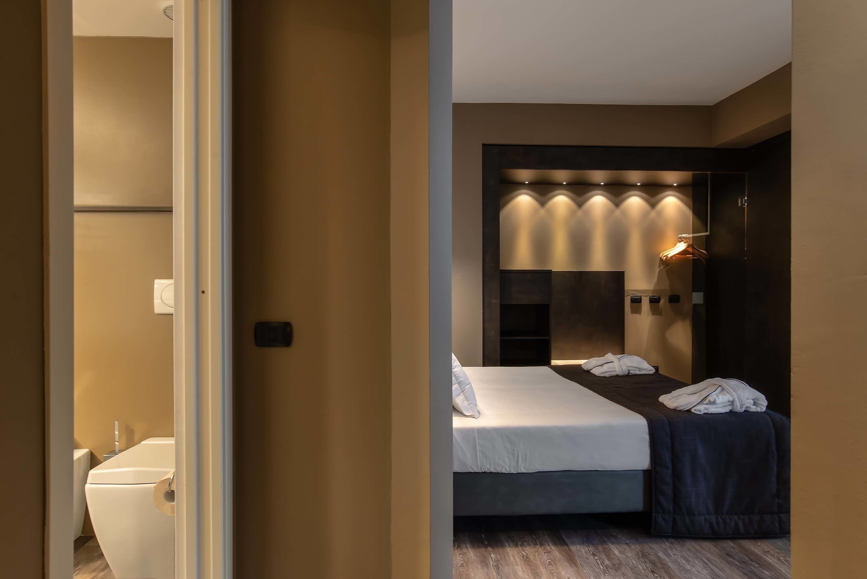 A modern hotel room with a large bed, a bedside table, and a built-in wardrobe.