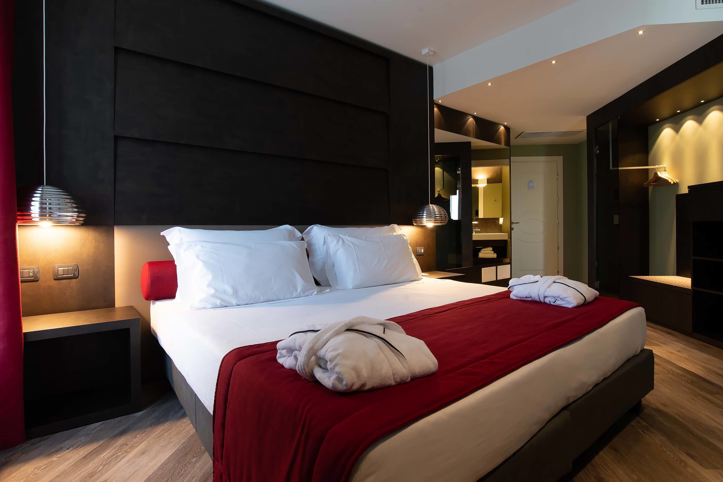 Et moderne hotelværelse med en stor seng, et rødt pled og et pænt foldet hvidt håndklæde.
