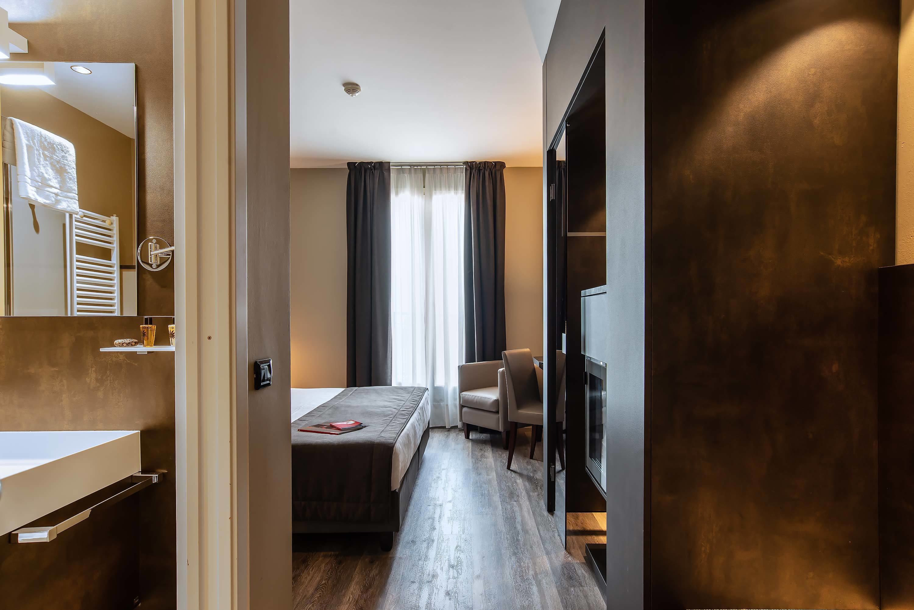 Ein Hotelzimmer mit Bett, Stuhl, Fernseher, Spiegel und einem Badezimmer mit Handtuchhalter.