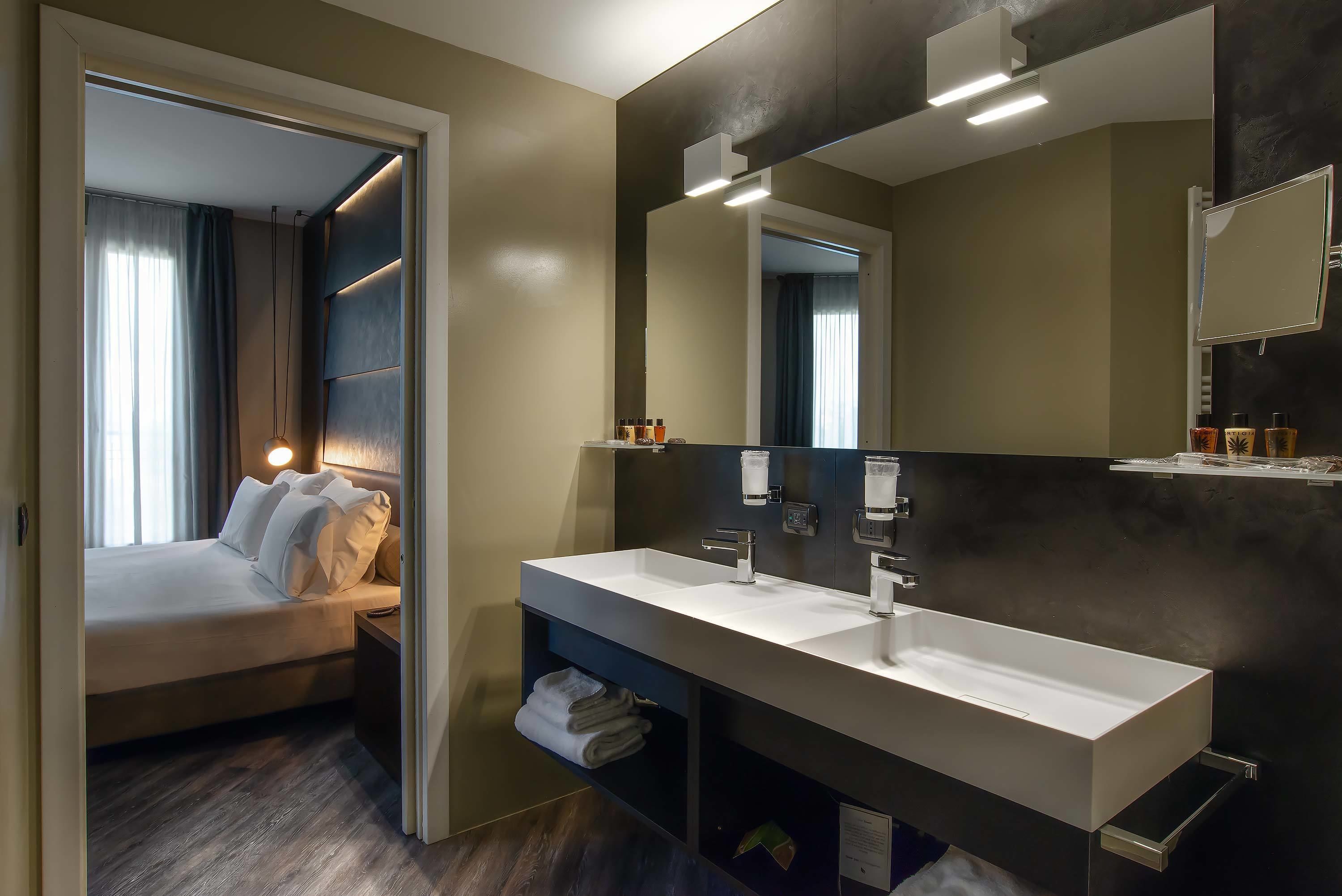 Una habitación de hotel moderna con una cama grande, un lavamanos doble y un espejo.
