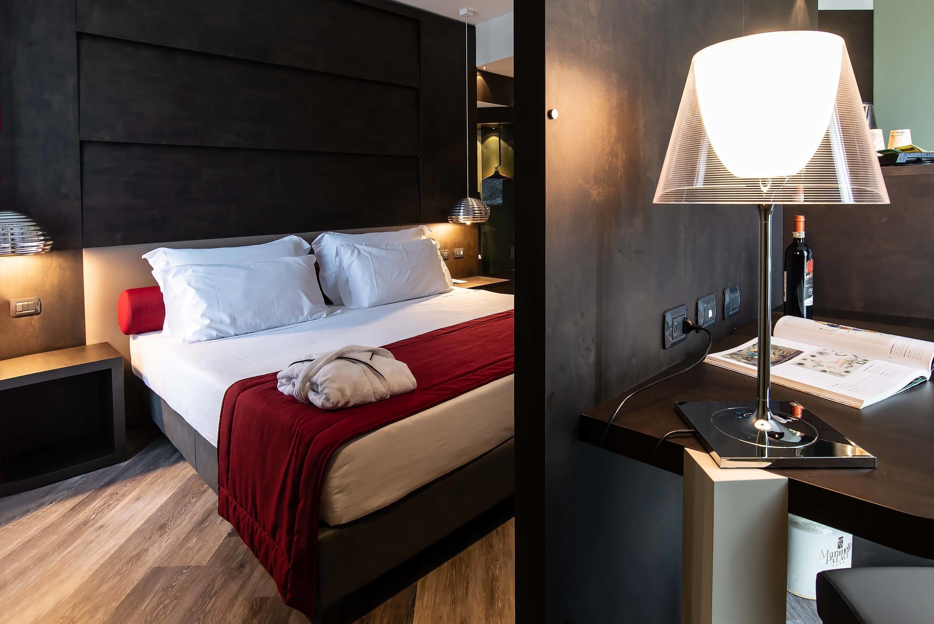 Una habitación de hotel moderna con una cama, lámparas de noche, un escritorio con lámpara y una botella.