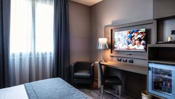 Ein Hotelzimmer mit Bett, Schreibtisch, Stuhl, Fernseher und Minibar.