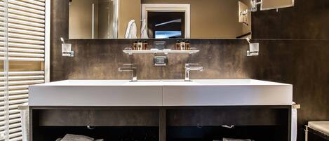 Une salle de bain moderne dotée d’un grand meuble-lavabo, de deux vasques et d’un miroir. On y trouve également des porte-serviettes et une étagère avec des articles de toilette.