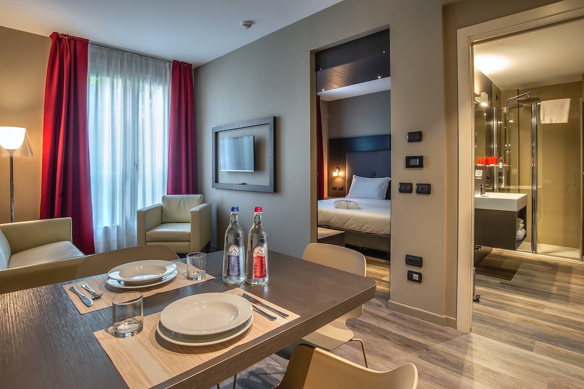 A hotel room with a dining area, a bed, a TV, and a bathroom.