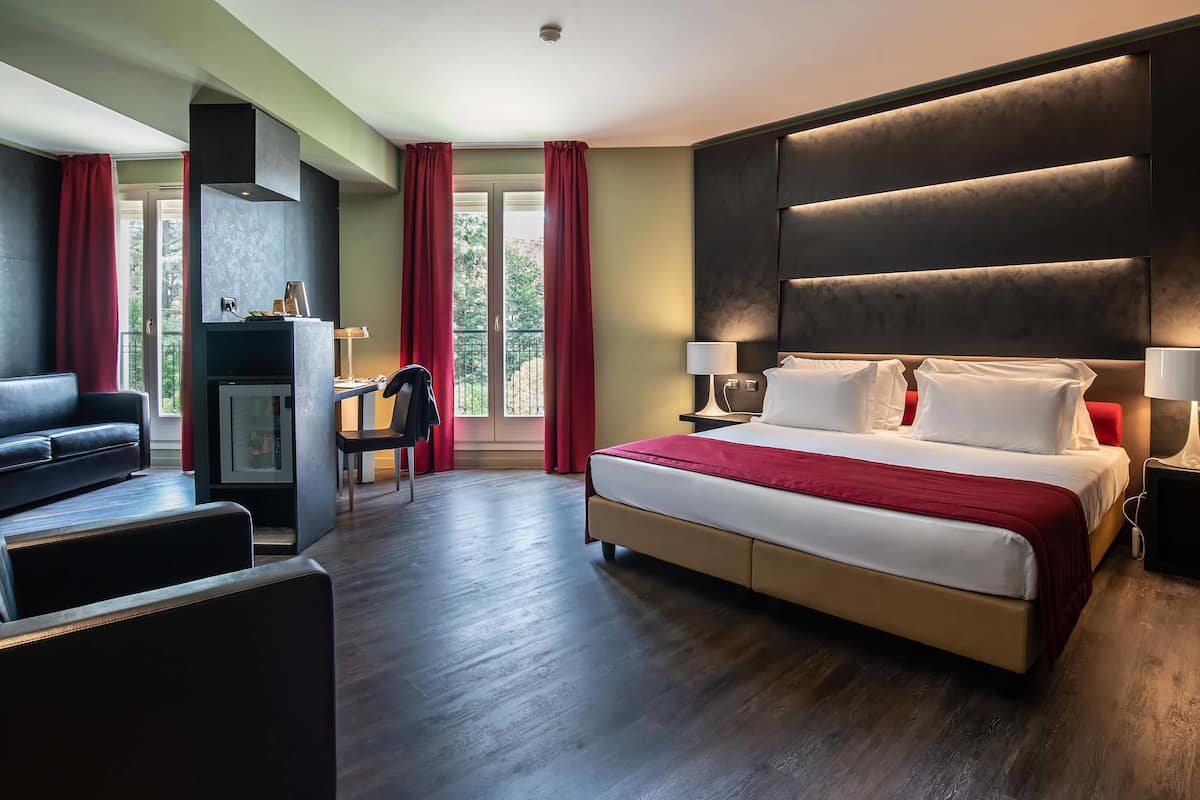 A hotel room with a large bed, a desk, a chair, and a view of the outdoors through a window.