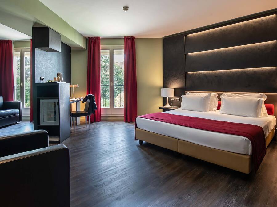 A hotel room with a large bed, a desk, a chair, and a view of the outdoors through a window.