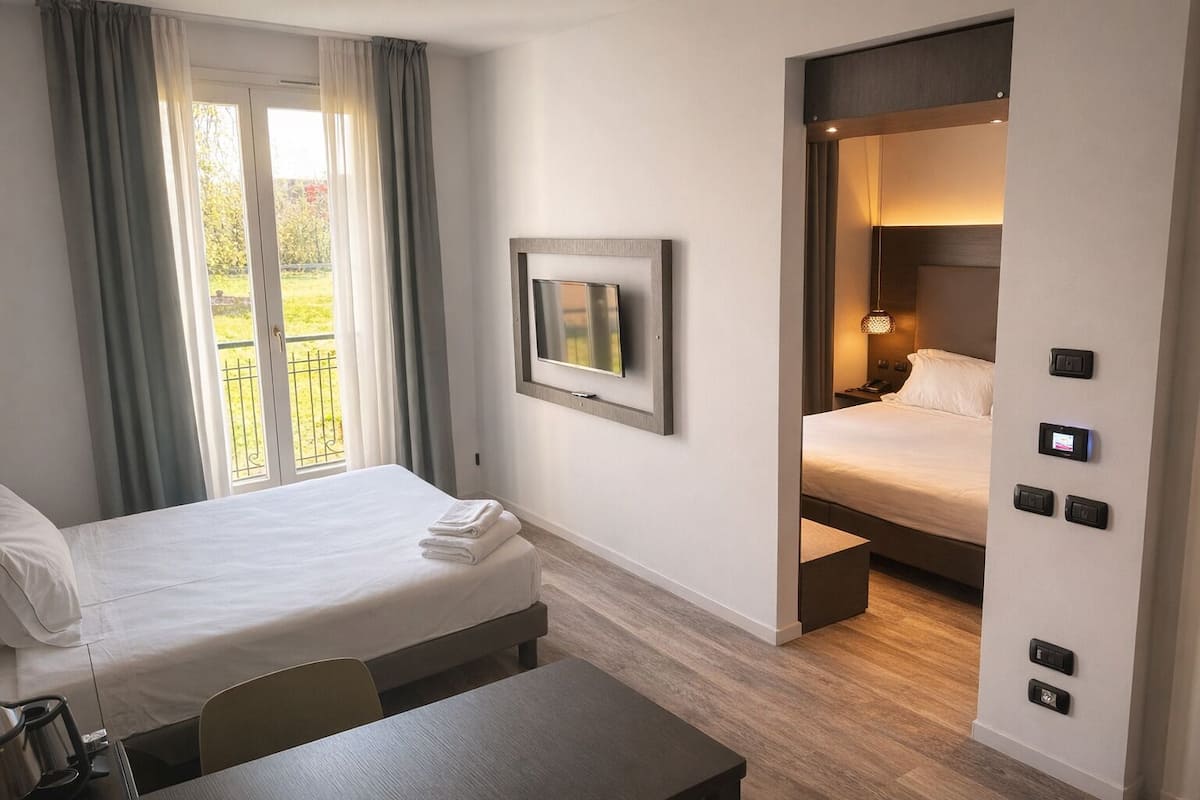 A hotel room with a bed, a desk, a chair, a TV, and a balcony with curtains.