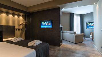 Una habitación de hotel moderna con una cama grande, una zona de estar y dos televisores de pantalla plana montados en la pared.