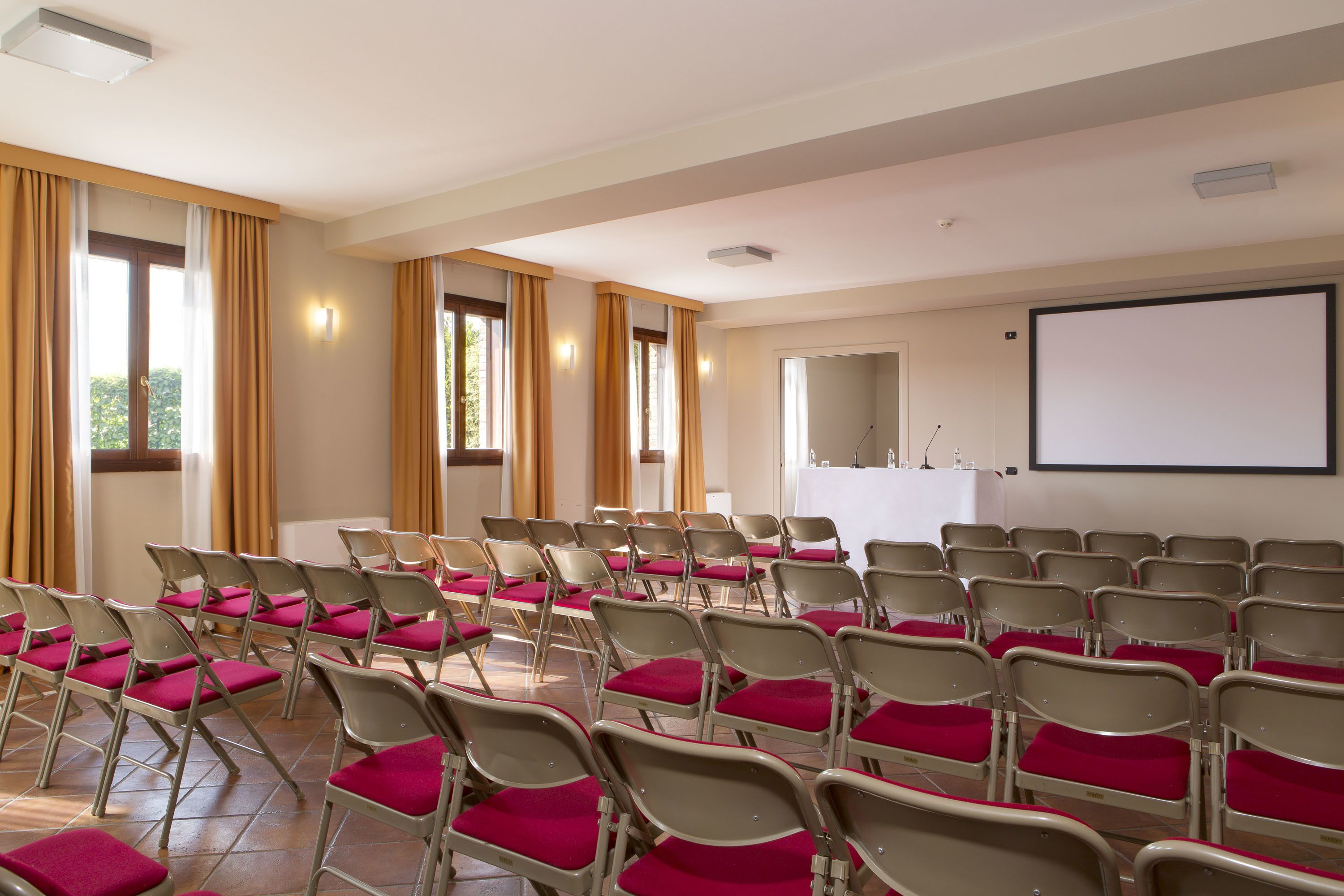 A conference room with rows of chairs, a whiteboard, and a projection screen.