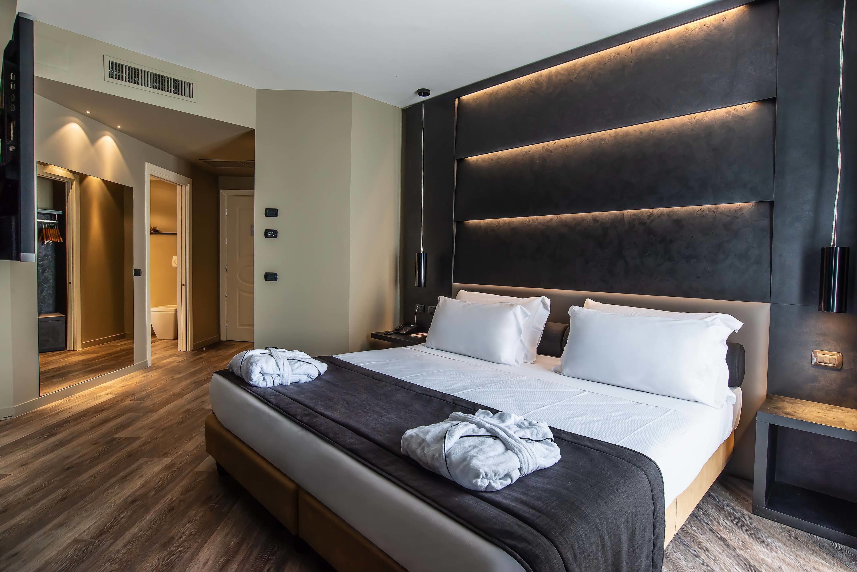 Ein modernes Hotelzimmer mit einem großen Bett, einem dunklen Kopfteil und Holzboden.