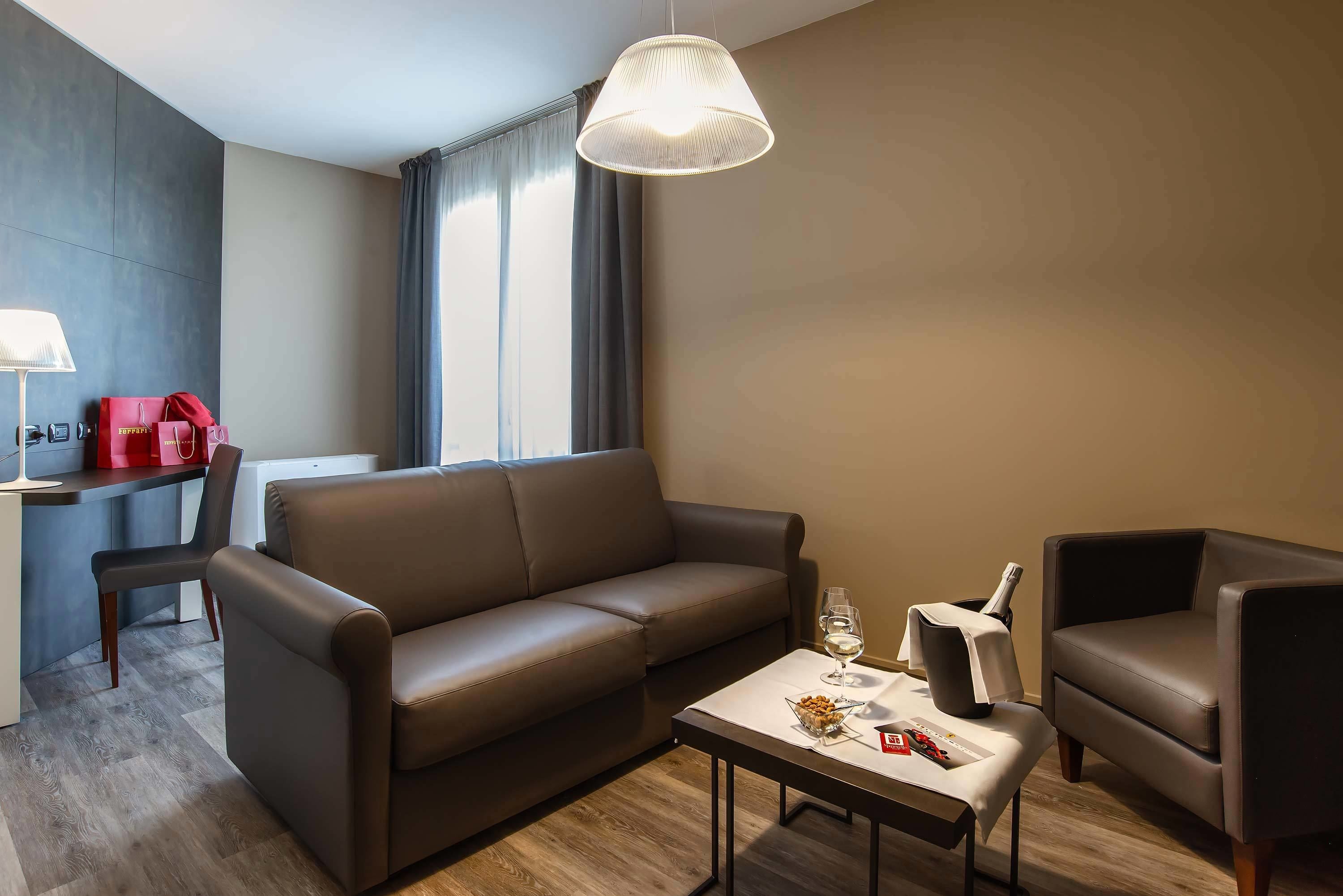 Una sala de estar moderna con un sofá de cuero marrón, una mesita con una copa de vino y una lámpara.