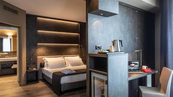 A modern hotel room with a bed, a desk with a laptop, a chair, and a minibar.