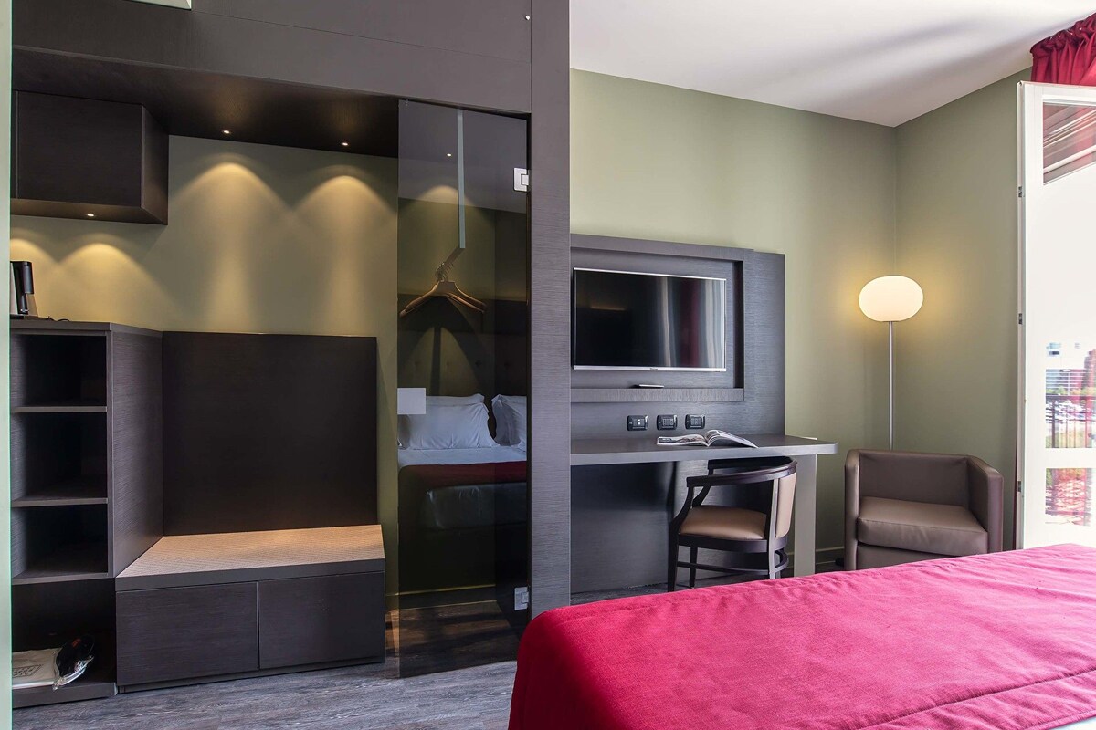 A hotel room with a bed, a desk with a TV, a chair, and a wardrobe.