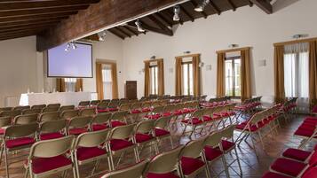 Un salón de conferencias con filas de sillas plegables, un atril y una pantalla grande.