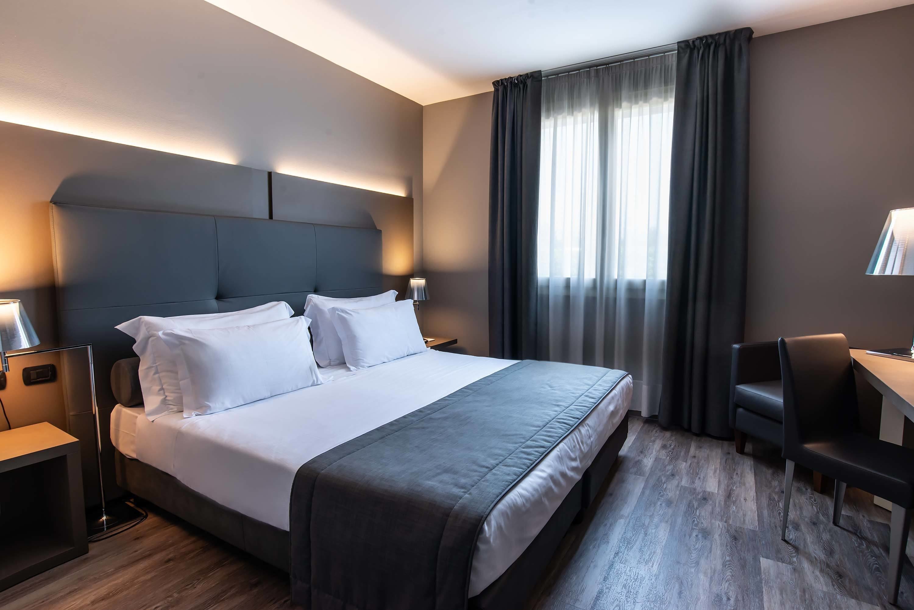 A modern hotel room with a large bed, bedside tables, a desk, and a chair.