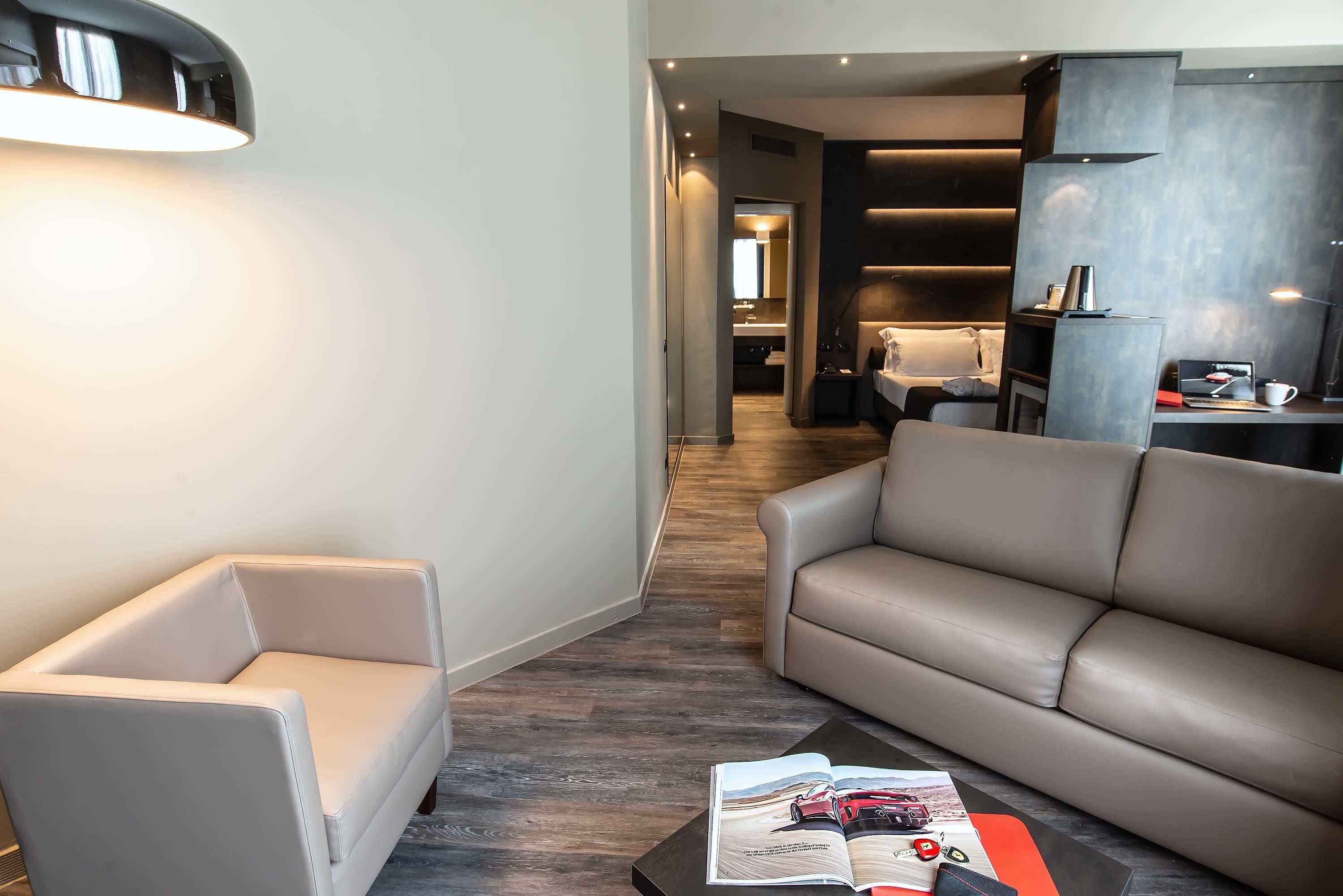 A modern living room with a sofa and armchair, a coffee table with magazines, and a hallway leading to a kitchen.