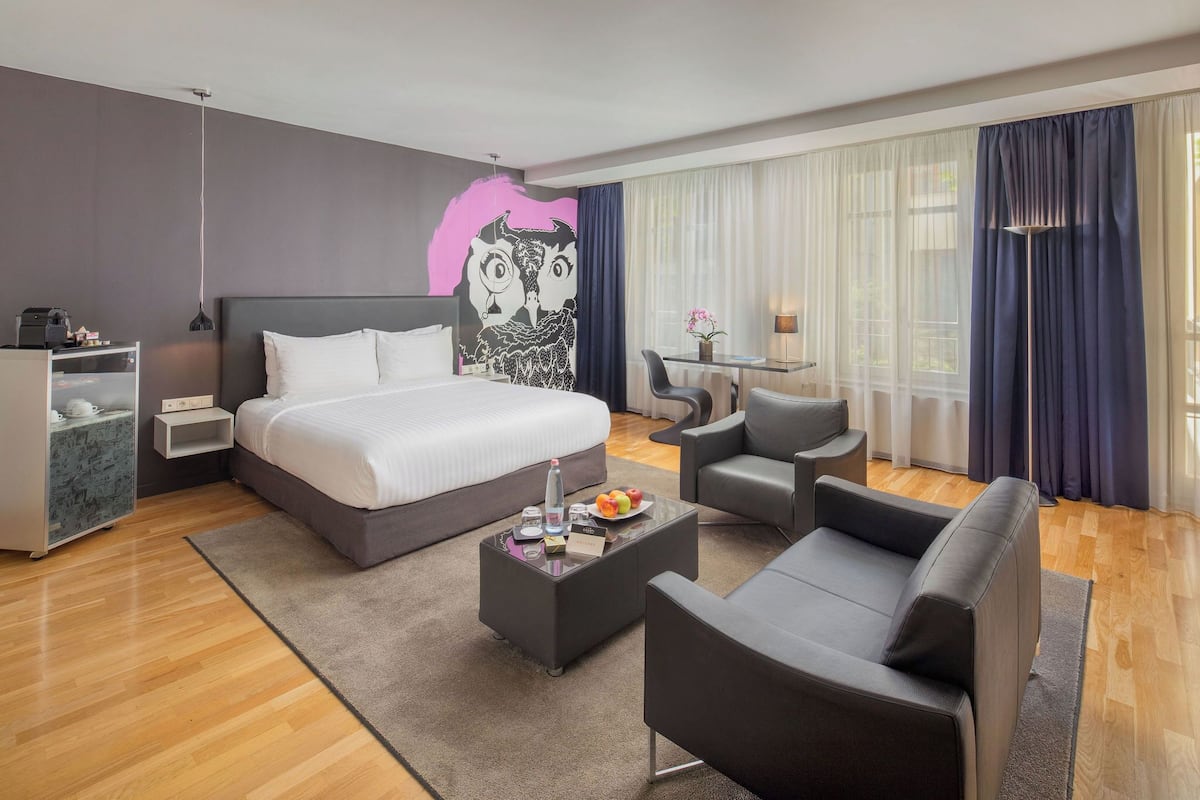 Moderni hotellihuone, jossa on suuri sänky, työpöytä, tuoli ja sohva.